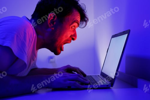Preview: Man shouts at laptop screen in dark room with blue lighting