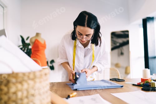 Preview: Concentrated female tailor cutting cloth with scissors