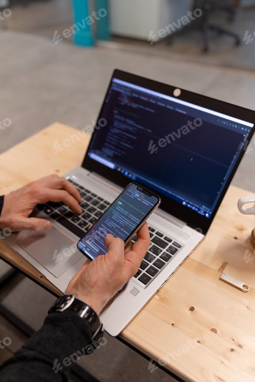 Preview: A programmer checking code on smartphone and lap top, testing
