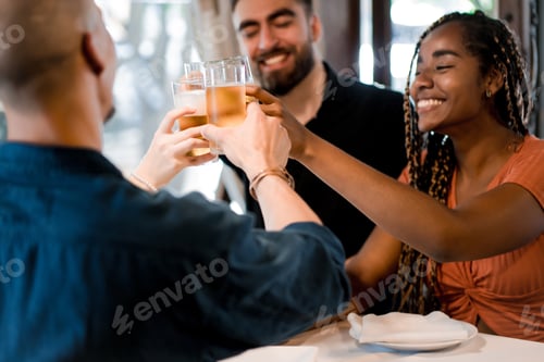 Preview: Group of friends toasting with beer glasses at a restaurant.