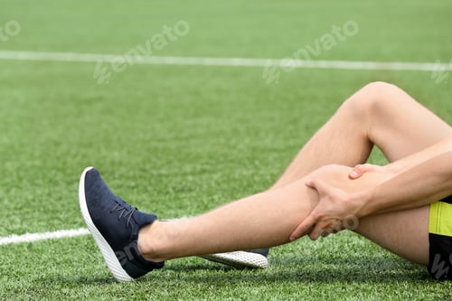 Preview: Man in sportswear suffering from knee pain at soccer field, closeup
