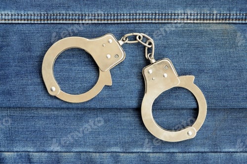 Preview: Police steel handcuffs lying on dark blue jeans background