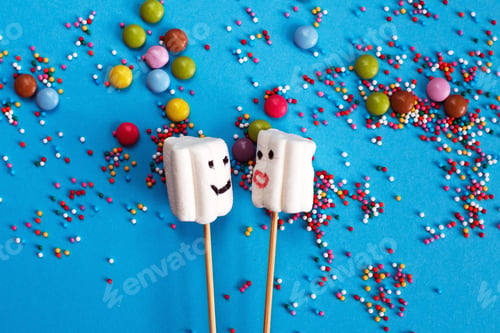 Preview: marshmallows on wooden skewers with color sweets on blue background.