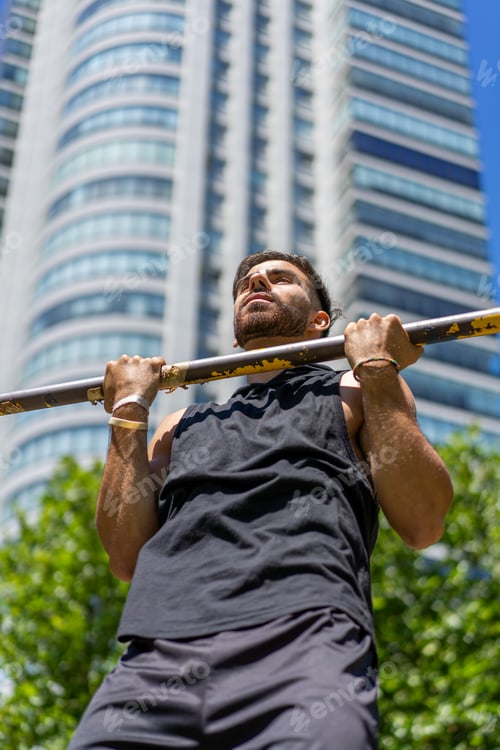 Preview: Young athlete performing pull-ups on outdoor gym bars