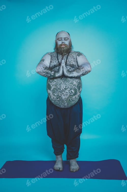 Preview: Hipster man with tattoos doing yoga and meditation exercises in the morning