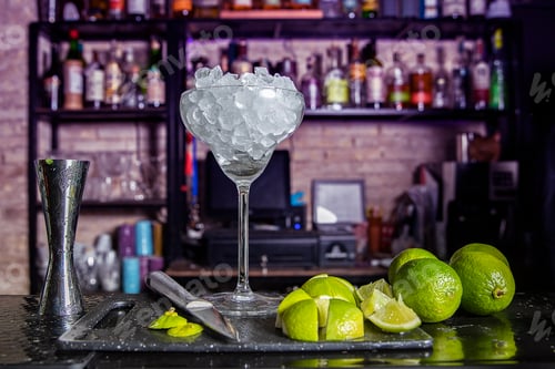 Preview: still life with a cocktail glass full of ice cubes and limes placed on the bar of a pub