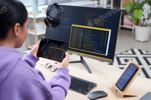 Preview: Female IT programmer holding tablet and writing code at workplace