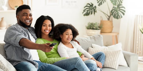 Preview: Smiling african american family relaxing and watching tv in living room