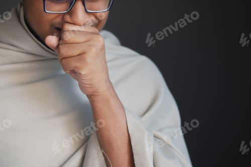 Preview: Mature man in blanket coughing while sited on bed