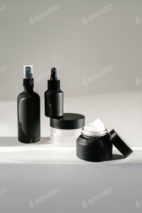 Preview: Black cosmetic bottles on a background flooded with sunlight.