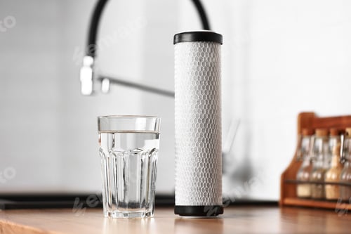 Preview: A glass of clean fresh water and carbon filter cartridge on wooden table in a kitchen interior.