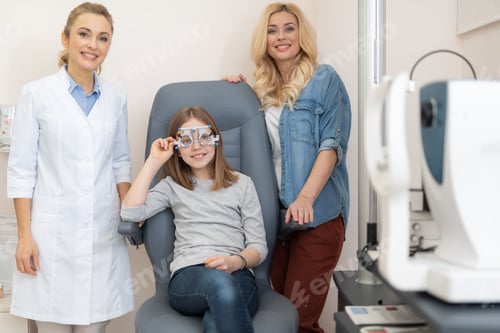 Preview: Portrait Of Adorable Child In Optical Trial Frame Sitting In Chair While Her Mother And