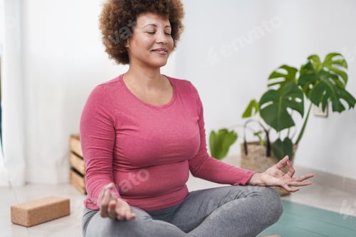 Preview: Mature african woman doing yoga meditation at home - Healthy lifestyle concept