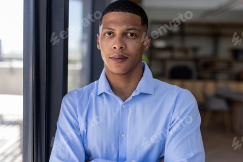 Preview: Confident professional in blue shirt standing by office window, looking determined