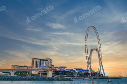 Preview: Low angle shot of modern design of a building with a huge Ferris wheel at Bluewaters island in Dubai