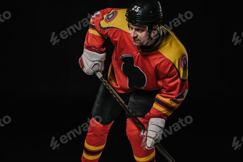 Preview: professional hockey player in protective sportswear holding hockey stick and looking away isolated