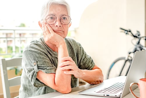 Preview: Pensive mature retired senior woman looking in distance sitting outdoors on terrace using laptop