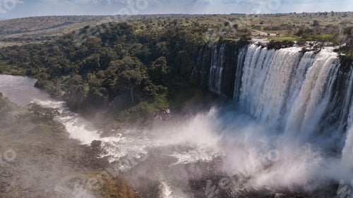 Preview: Kalandula Waterfall cascading in Angola with lush greenery and mist on a bright day