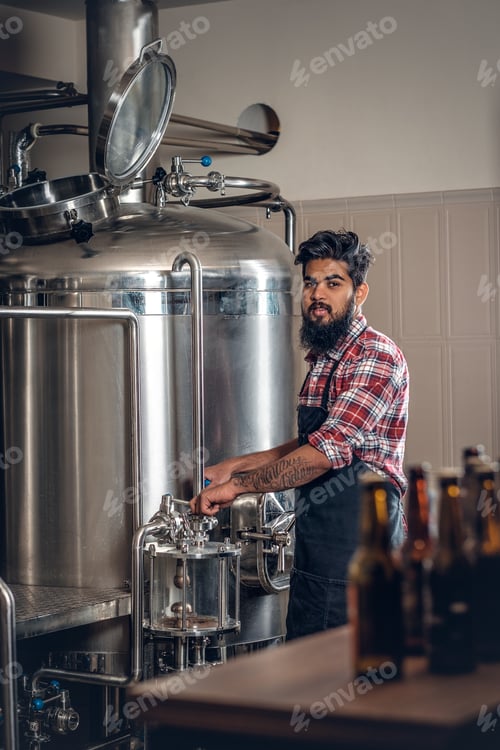 Preview: Indianr male manufacturer presenting craft beer in the microbrewery.