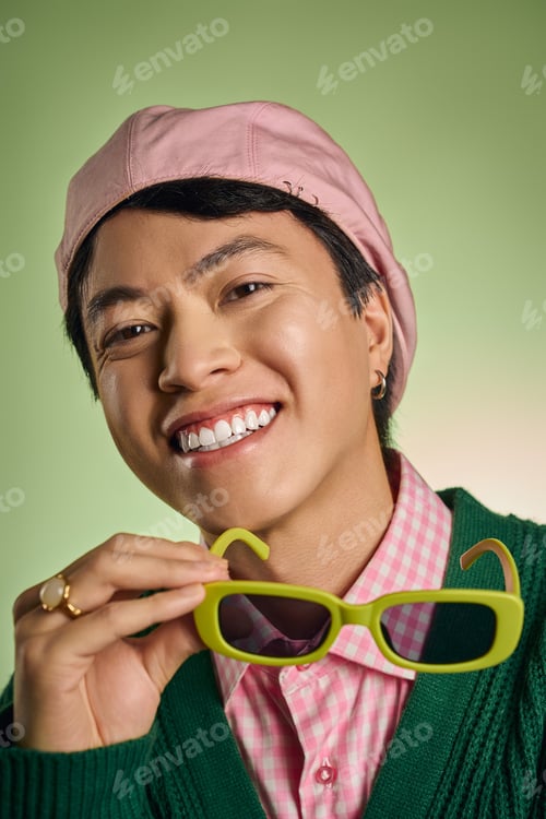 Preview: Stylish asian man showcasing trendy fashion in vibrant green studio setting