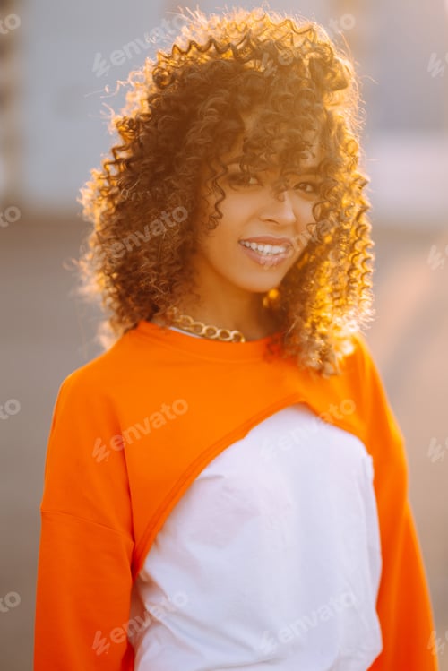 Preview: Dancer dancing in street at sunset. Beautiful African American woman with curly hair in orange suit.
