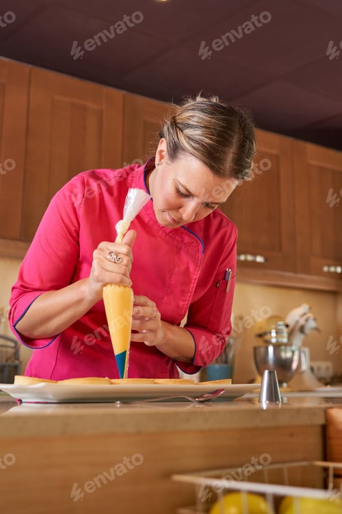 Preview: Female pastry chef making peaks of cream on tarts