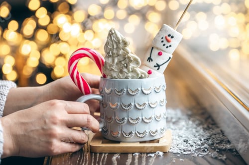 Preview: Cup with a hot drink, marshmallows and sweets in female hands, close up.