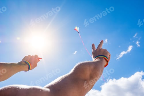 Preview: close up and portrait of arms and hands up wearing bracelet of lgtb colors and flying a kite