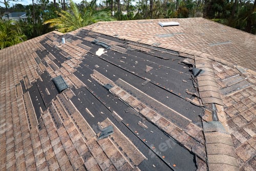Preview: Wind damaged house roof with missing asphalt shingles after hurricane Ian in Florida.