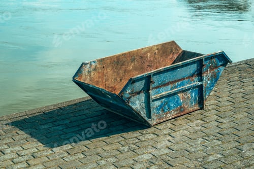 Preview: Old worn skip container on riverbank