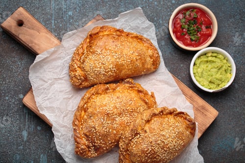 Preview: Delicious baked empanadas with sesame seeds served on wooden board with sauces, traditional Spanish