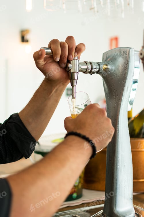 Preview: Barman hands at beer tap pouring a draught lager beer serving in a restaurant or pub