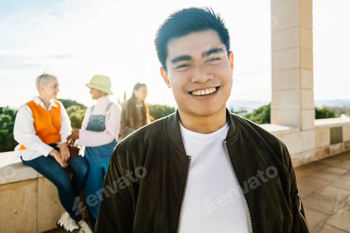Preview: Young confident asian man smiling at camera while standing with multiracial friends outdoors