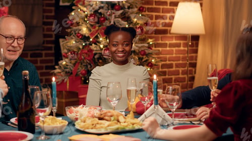 Preview: Young african american woman smiling heartily at camera while enjoying Christmas dinner with family