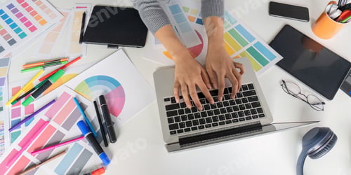 Preview: Creative Graphic Designer Working on Laptop with Color Palettes and Design Tools on Desk