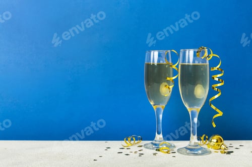 Preview: Champagne glasses and christmas decor on colored holiday background. Flat lay New Year decorations