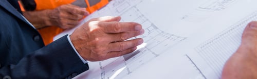 Preview: panoramic shot of businessman gesturing near blueprint and constructors