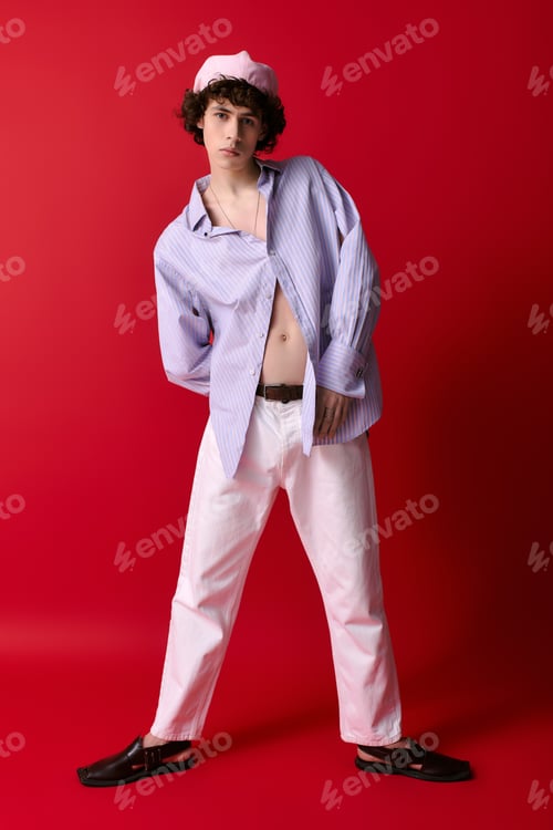 Preview: Young stylish man showcases bold fashion against vibrant red backdrop in a playful pose