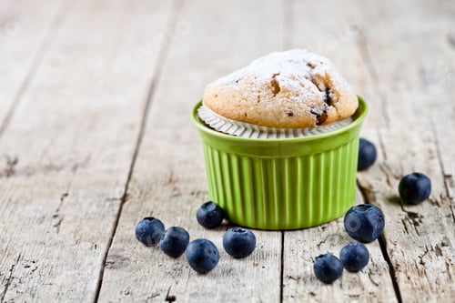 Preview: Homemade fresh muffin on ceramic green bowl with blueberries on rustic wooden table.