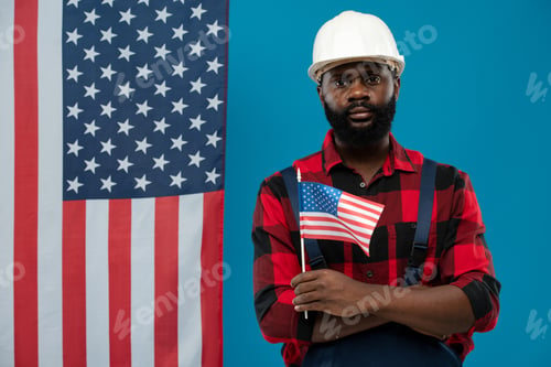 Preview: Young bearded African-american worker in flannel and hardhat holding flag