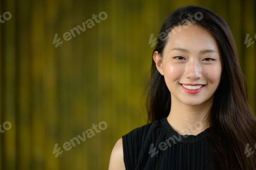 Preview: Happy young beautiful Asian businesswoman against bamboo fence