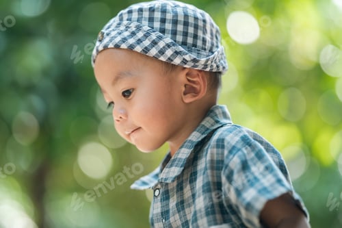 Preview: Curious baby boy outdoor toddler portrait plaid shirt summer light green bokeh background