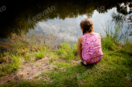 Preview: Rear view of girl crouching on riverbank looking water