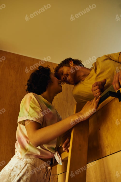 Preview: happy asian woman climbing wooden ladder of bunk bed near redhead boyfriend, weekend getaway