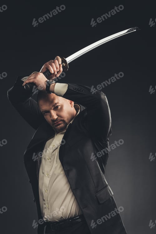 Preview: serious mature man in suit with katana sword isolated on black