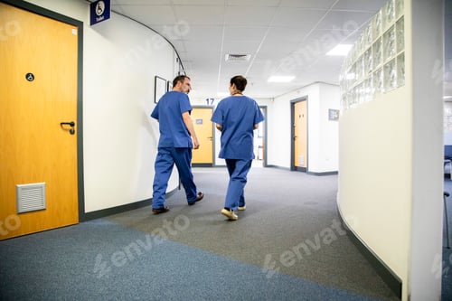 Preview: Two healthcare workers walking in a hospital corridor, medical practice UK
