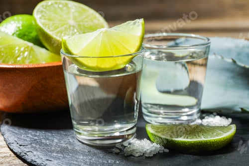 Vista previa: Chupitos de tequila con rodajas de lima, sal y hojas de agave sobre la mesa, primer plano