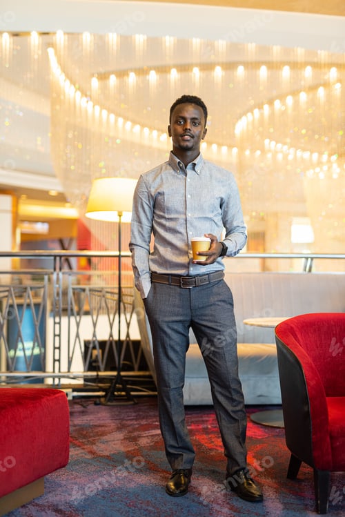 Preview: Portrait of handsome young African man having coffee break indoors