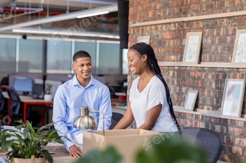 Preview: Colleagues in office smiling and discussing project near desk with plants