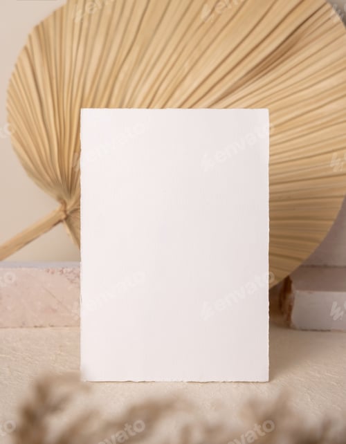 Preview: Blank card near beige travertine stones against dry beige palm leaf close up, greeting mockup